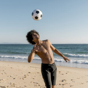 jovem-atleta-negro-jogando-bola-de-futebol-na-praia